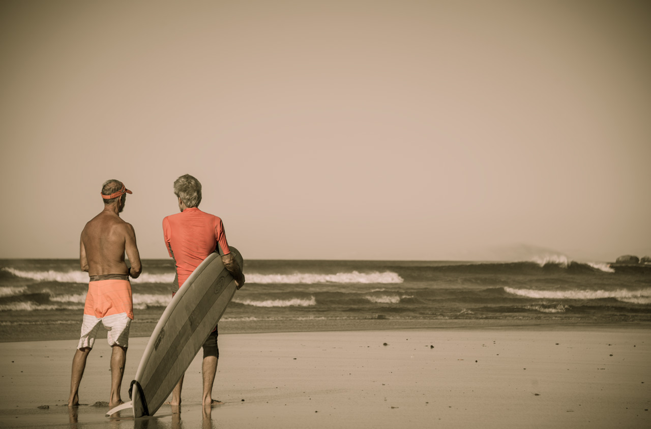 Two surfers standing on a beach in Nosara holding surfboards, looking at the waves