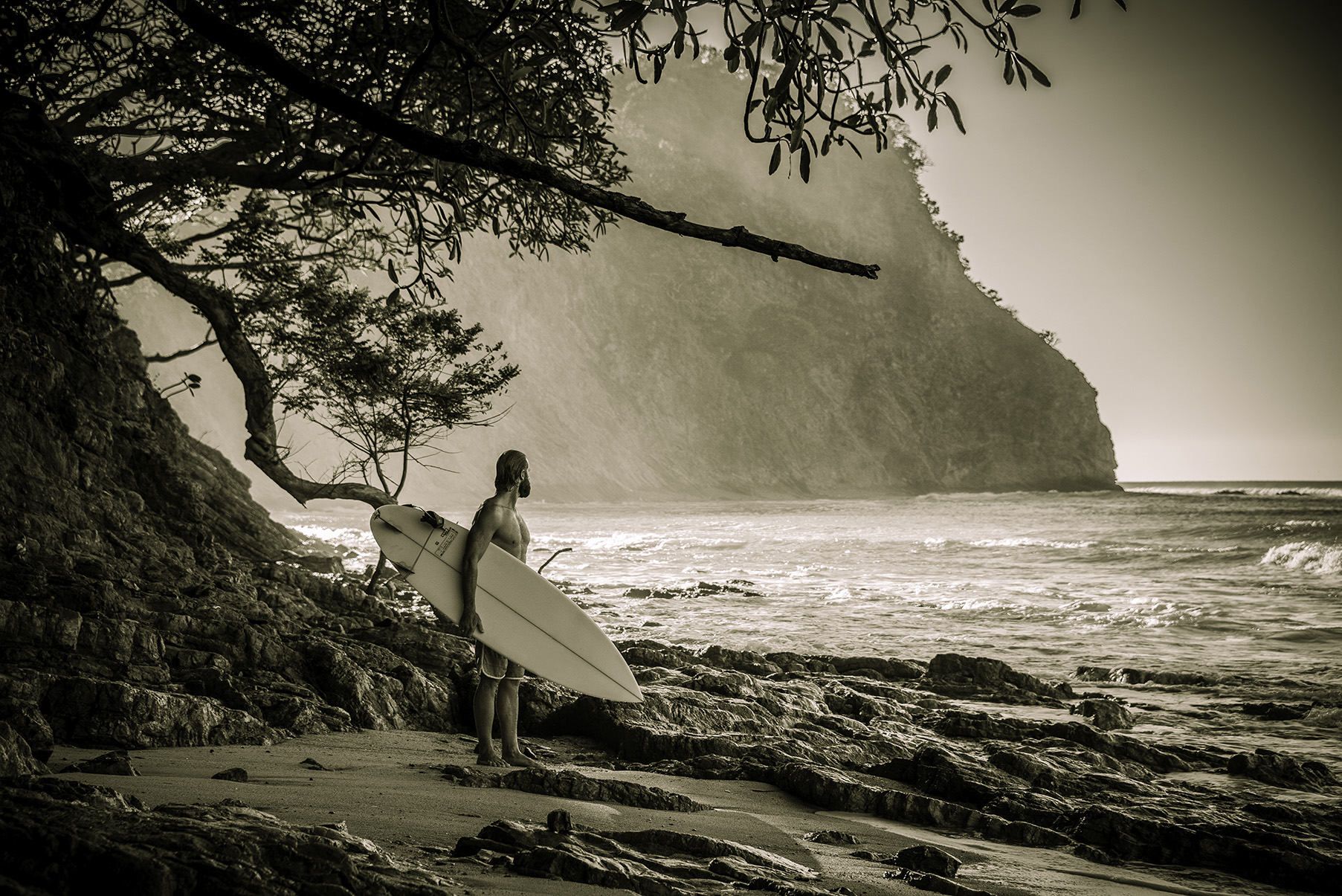 A surfer on a rocky Costa Rica beach gazing at the waves