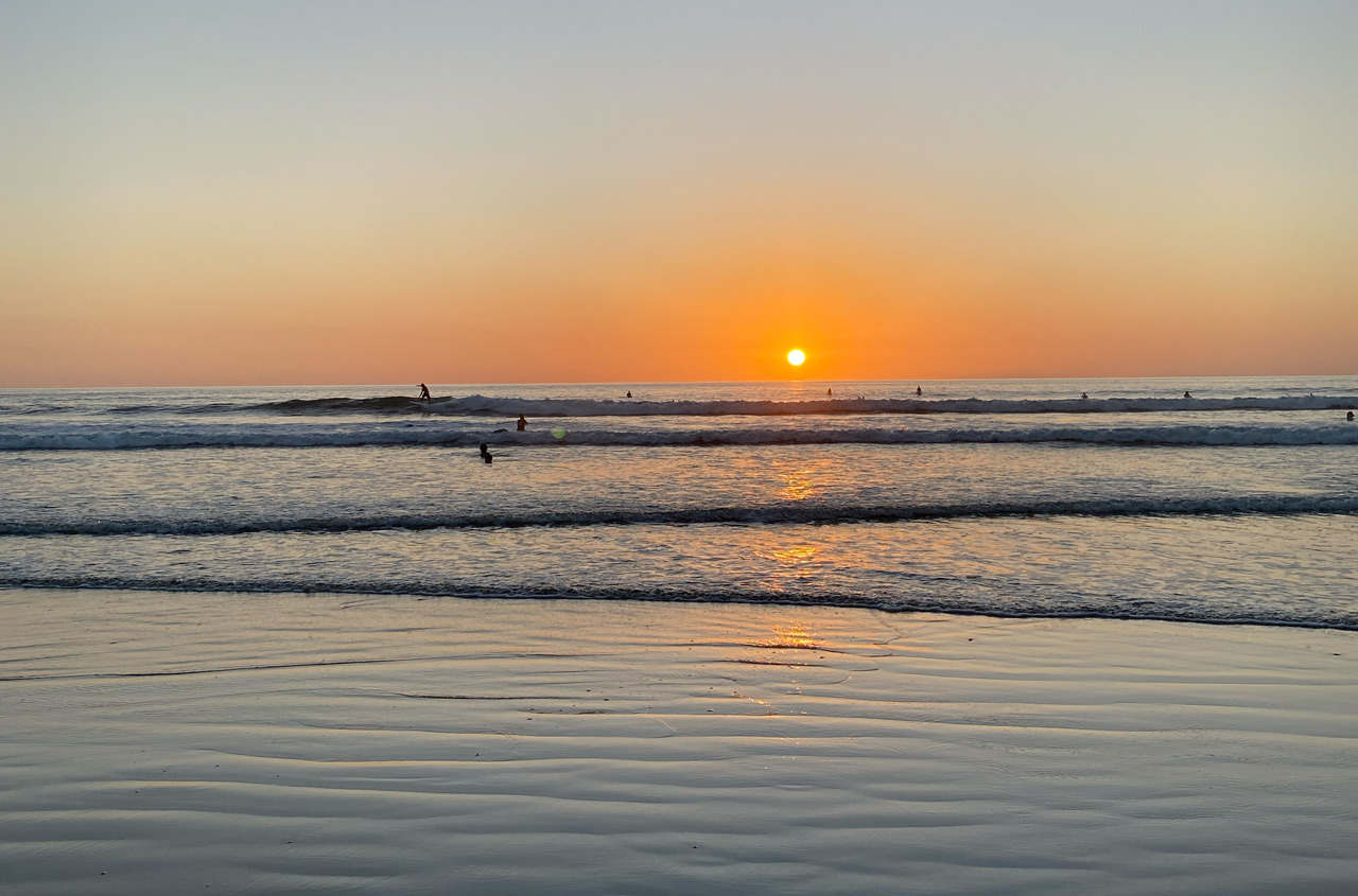 Golden sunset over a calm ocean with surfers riding gentle waves at a beach in Nosara